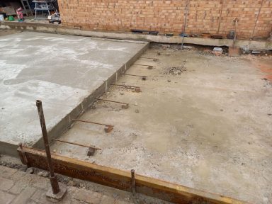 Concrete foundation with exposed rebar, building site in the background.