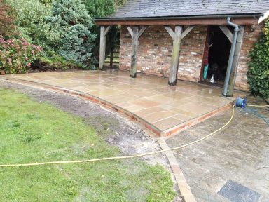 A newly laid stone patio adjacent to a brick building and landscaped garden.