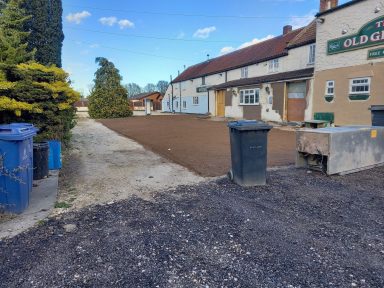 Wide view of a gravel area beside buildings and waste bins under a blue sky.
