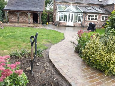 Garden pathway leading to a conservatory, with greenery and a brick border.