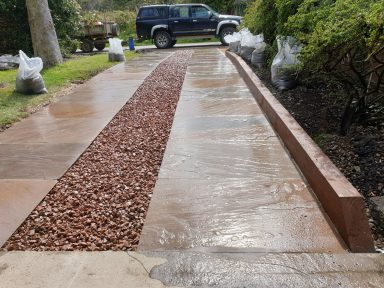 Driveway with a gravel strip, bordered by concrete edges and surrounded by greenery.
