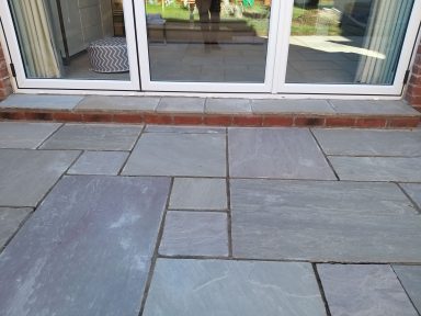 Paved patio area with varying stone colours leading to sliding glass doors.