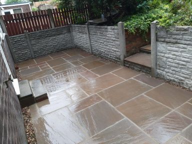 Paved outdoor patio area with stone slabs, surrounded by a low wall and greenery.