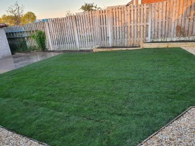 Well-maintained lawn surrounded by gravel and a wooden fence.