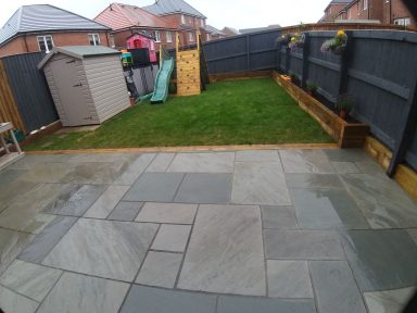 Paved garden area with a slide, shed, and green lawn surrounded by fences.