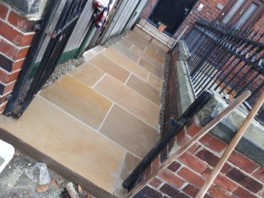 Pathway made of stone slabs between brick walls, leading to a black door.