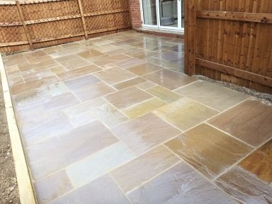 Paved patio area with various stone tiles, surrounded by wooden fencing.